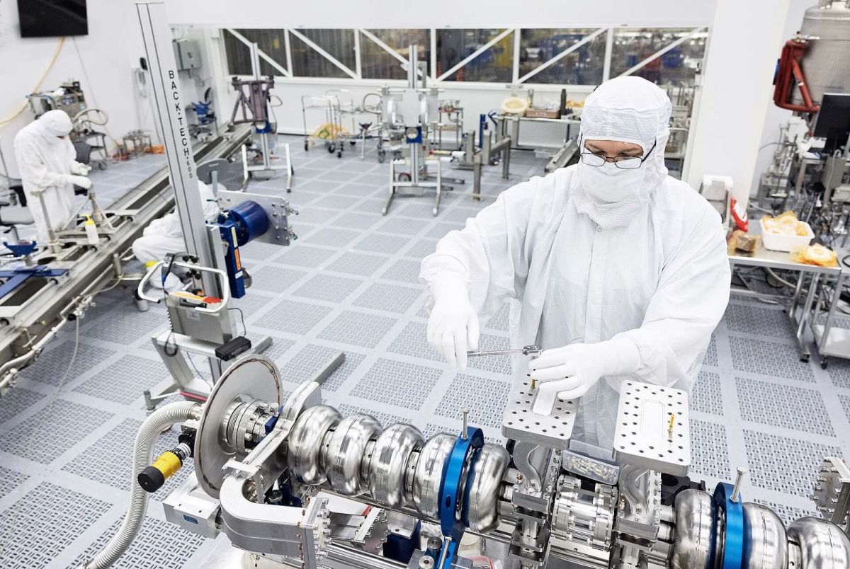 Technicians in cleanroom suits assembling precision equipment in a semiconductor-grade clean room