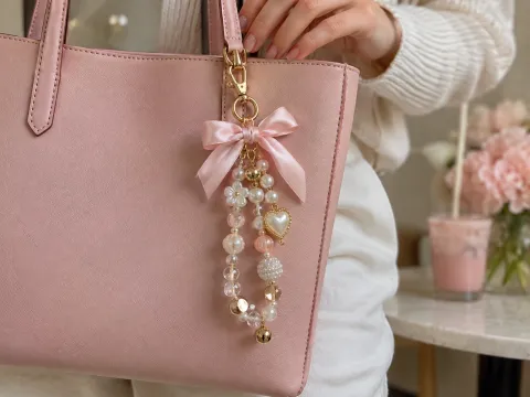 Illustrative AI image: a finished beaded charm with pearls and a bow hanging from a pastel tote bag
