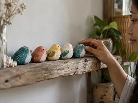 Illustrative AI image: five little painted bird stones lined up on a driftwood shelf